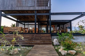 A modern building with a wooden deck, outdoor seating, and a garden area with rocks and plants.