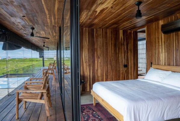 Une pièce en bois avec un lit, un mur en verre et un balcon équipé de chaises.