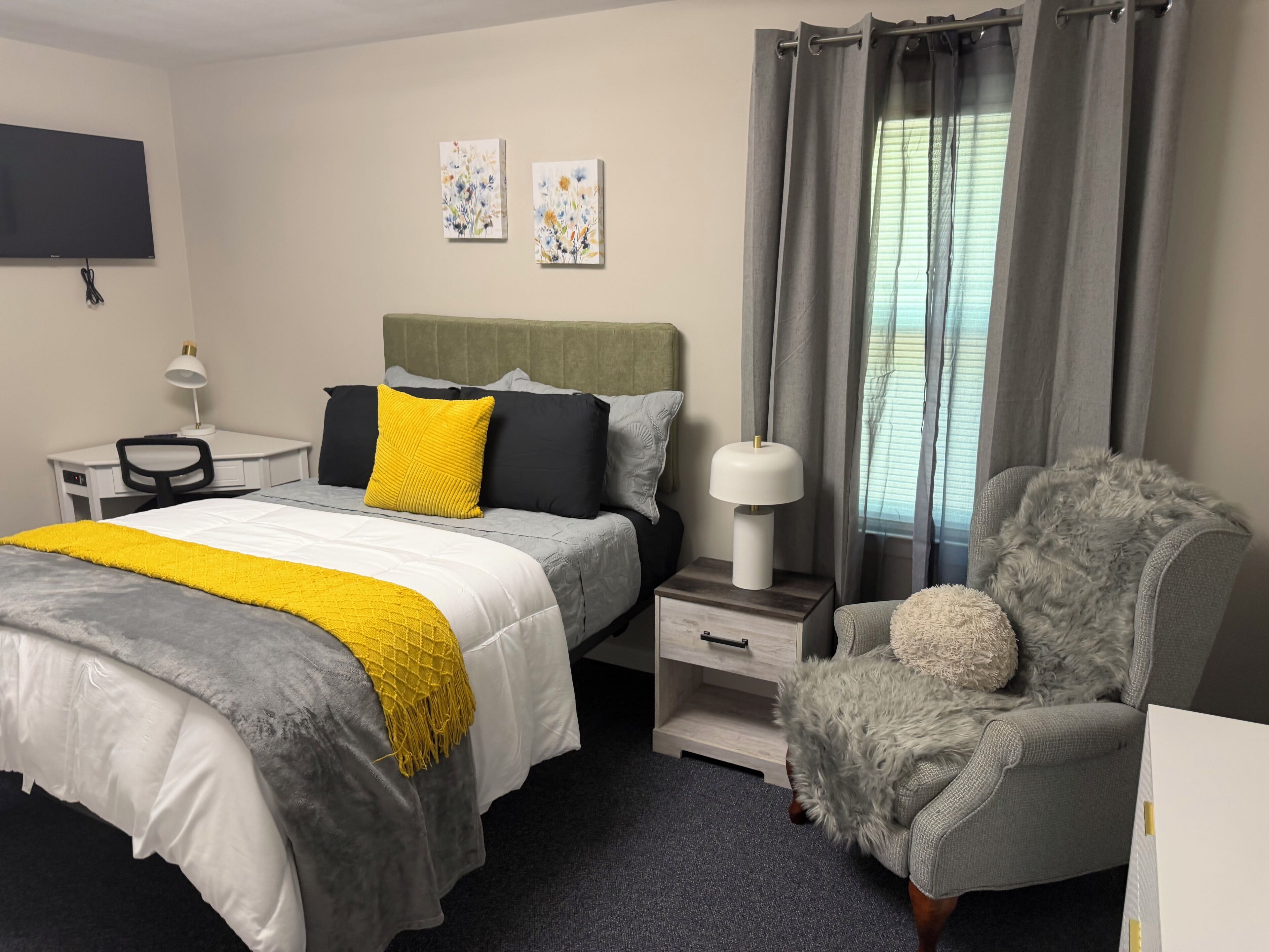 A hotel room with a bed, a desk, a chair, a lamp, and a TV.