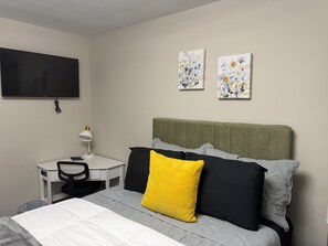 Ein Hotelzimmer mit einem Bett, einem Schreibtisch, einem Sessel, einem Fernseher und zwei Wandbildern.