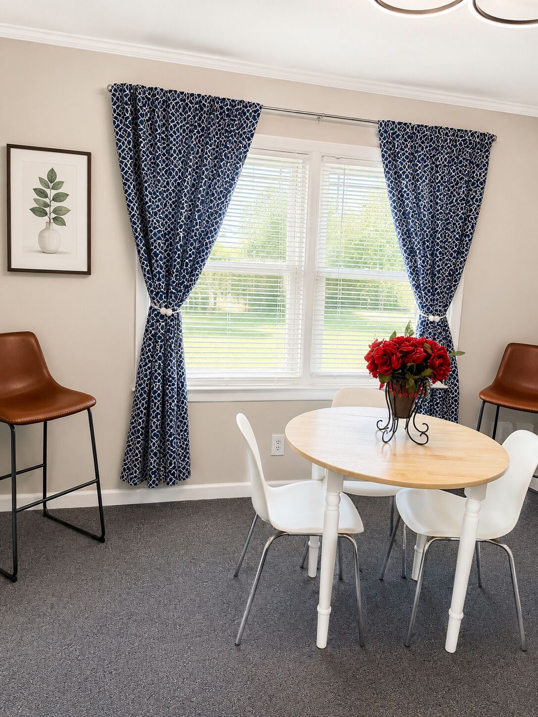 A dining area with a round table, white chairs, and a vase of red flowers.