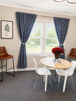 Ein Essbereich mit einem runden Tisch, weißen Stühlen und einer Vase mit roten Blumen.