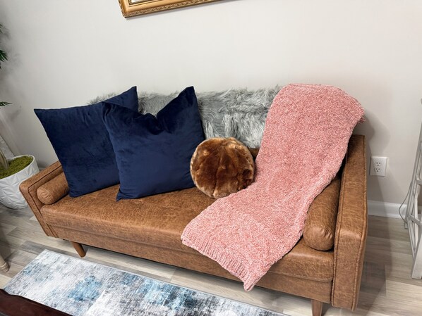 A brown leather sofa with a pink blanket and two dark blue pillows.