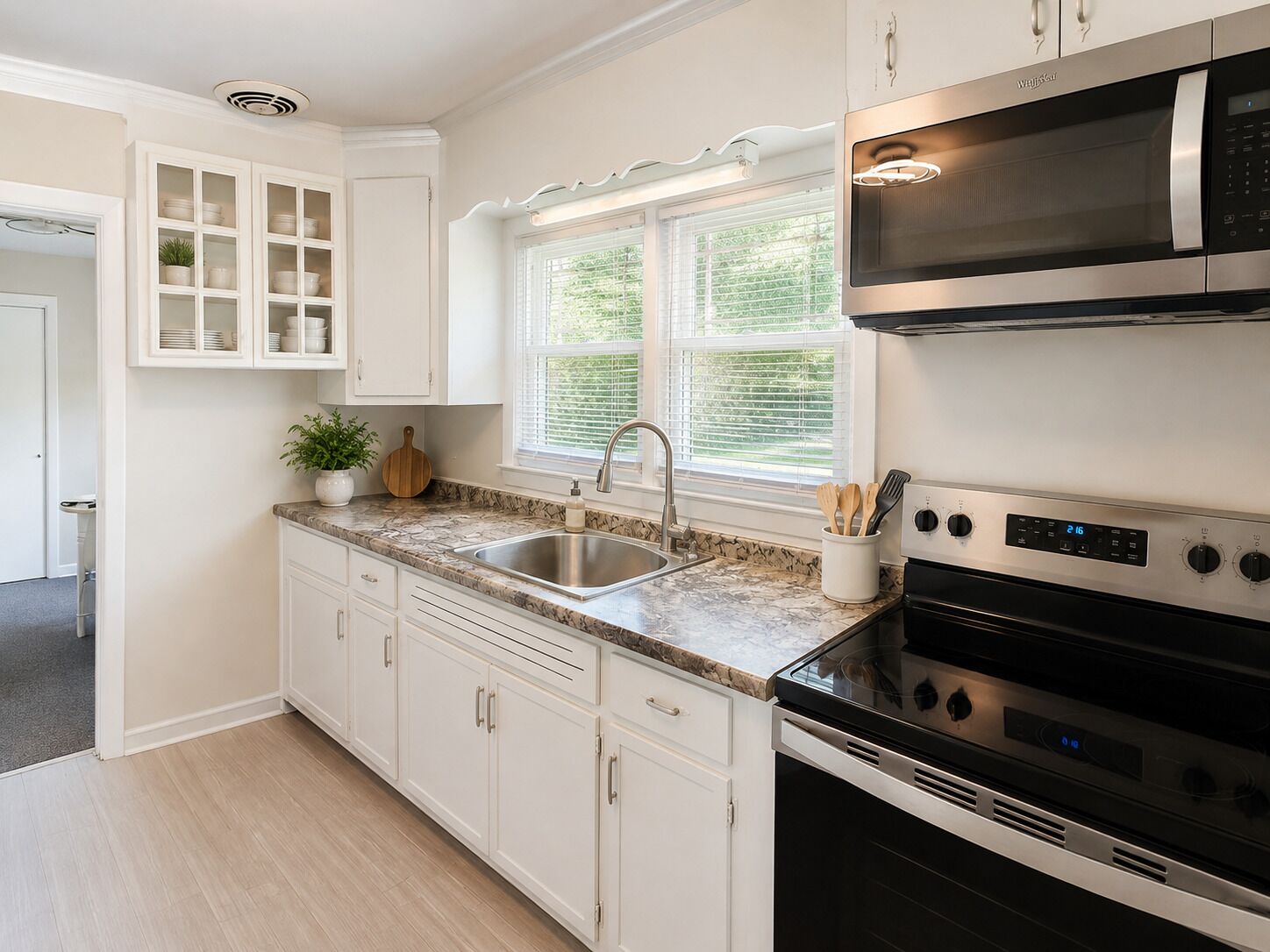A kitchen with white cabinets, a stainless steel sink, a microwave, and an oven.