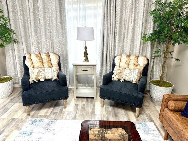 A living room with two armchairs, a side table with a lamp, a coffee table, and a potted plant.