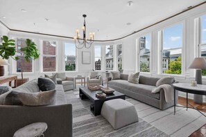A spacious living room with large windows, a chandelier, and a modern fireplace. - Lexington "Pent Hous" Prime Location 4Bdrm, 6 Beds (Lexington)