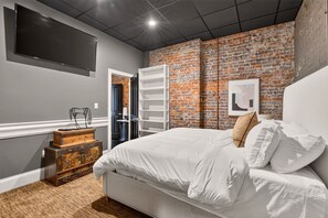 Un dormitorio con pared de ladrillo, cama, televisor y armario.