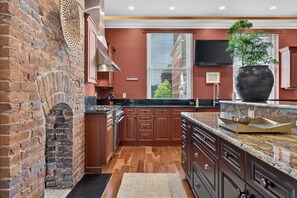 Une cuisine avec un mur en briques, des meubles en bois, une grande fenêtre et une plante en pot.