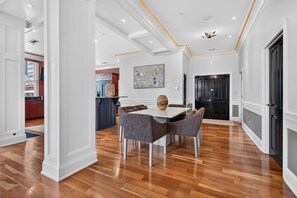 A spacious dining area with a wooden floor, a white table, and grey upholstered chairs.