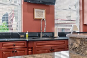 A kitchen with a black countertop, wooden cabinets, a stainless steel sink, and a framed picture on the wall.