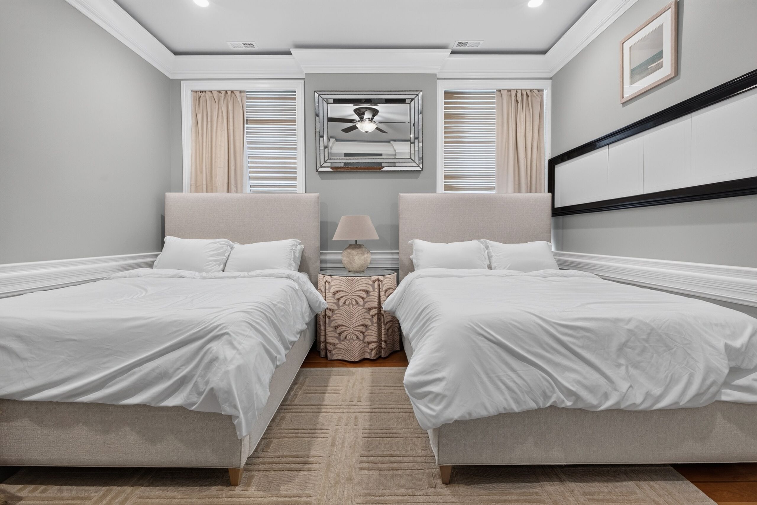 A hotel room with two beds, a nightstand, a lamp, and a ceiling fan.