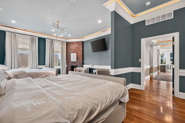 A modern bedroom with a large bed, a brick accent wall, a flat-screen TV, and a view of the outdoors.