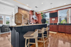 Una cocina moderna con una isla central, taburetes de bar, una pared de ladrillo y un ventanal grande.