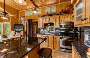 A wooden cabin interior with a kitchen featuring granite countertops, stainless steel appliances, and a large island with seating.