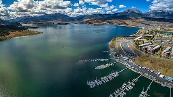 An aerial view of a coastal town with a marina, boats, and mountains in the background.