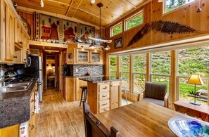 A wooden interior with a kitchen, dining area, and large windows overlooking greenery.