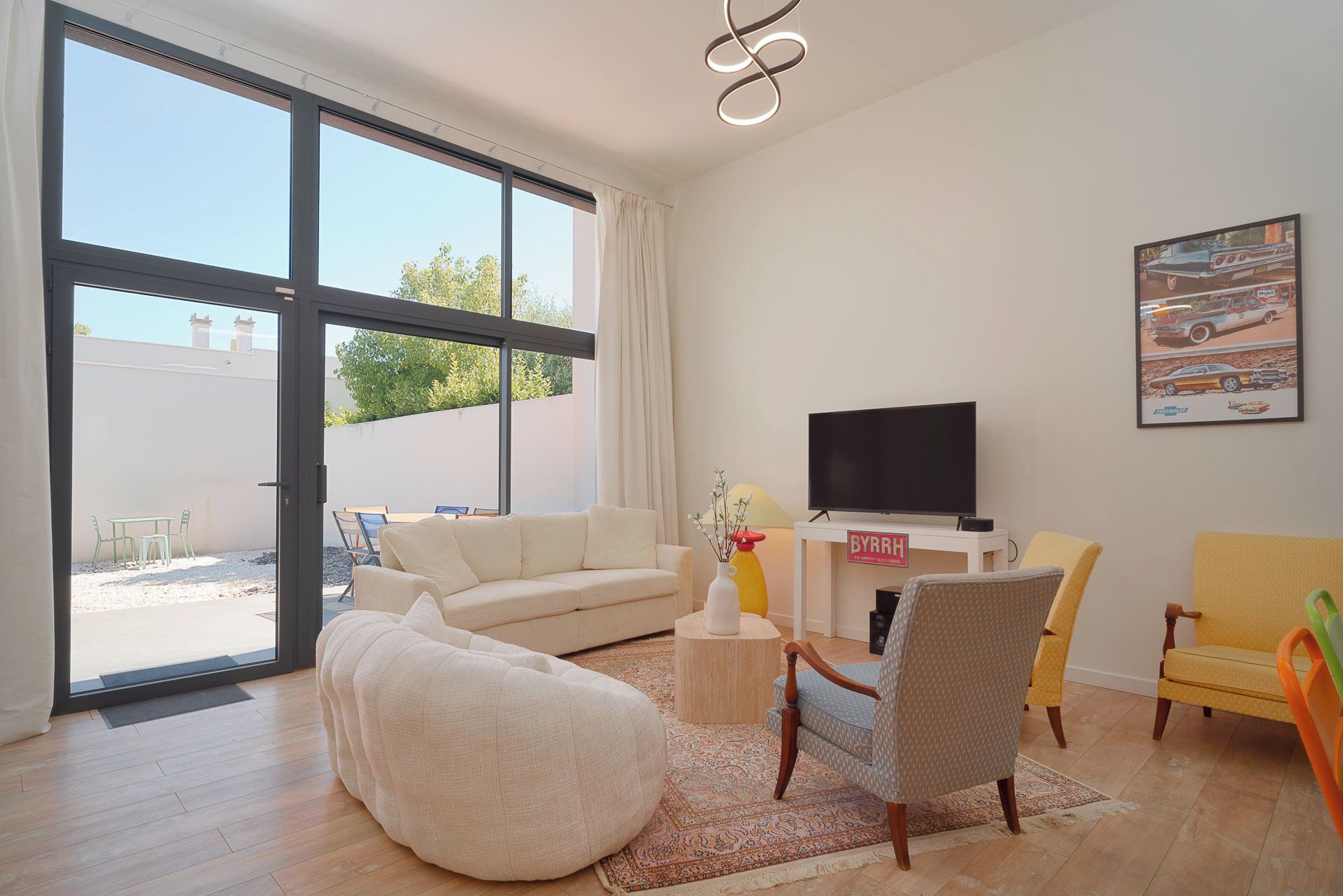 A modern living room with a sofa, chairs, a TV, and a large window.