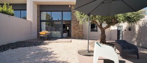 Una casa moderna con un patio, una mesa y una silla bajo un paraguas grande.