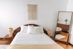 A neatly made bed with white linens, a wooden headboard, and a hanging macrame wall hanging. - Casa Suave Mar (Marinhas)