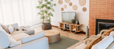 Una sala de estar con un sofá, un televisor sobre un mueble de madera, una planta en maceta y una chimenea.