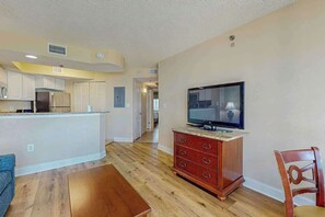 Un salon avec un plancher en bois, un téléviseur posé sur un meuble, une armoire en bois et une chaise.