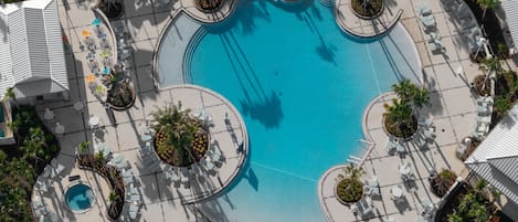 Vista aerea di un resort con piscina centrale, circondata da aree relax con sedie e tavoli, e palme.