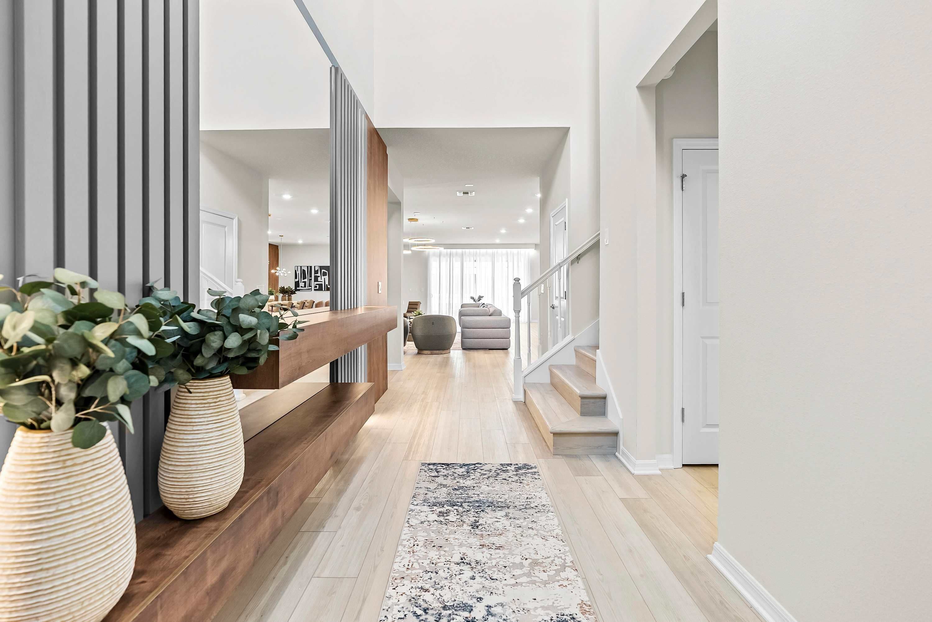 A modern hallway with a wooden bench, a black and white rug, and a staircase leading to another level.