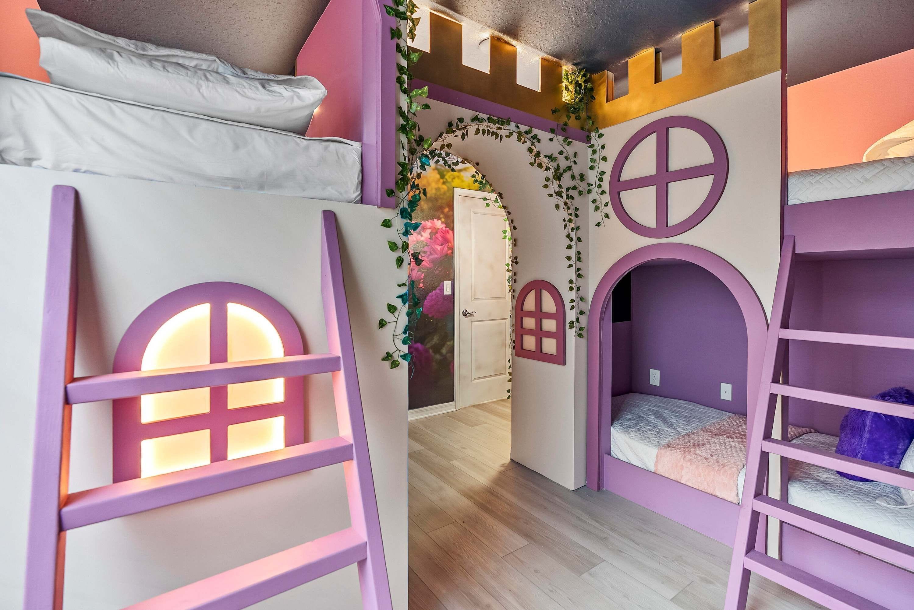 Una stanza giochi per bambini con letti a castello, una porta con finestra e decorazioni come edera e un fiore.