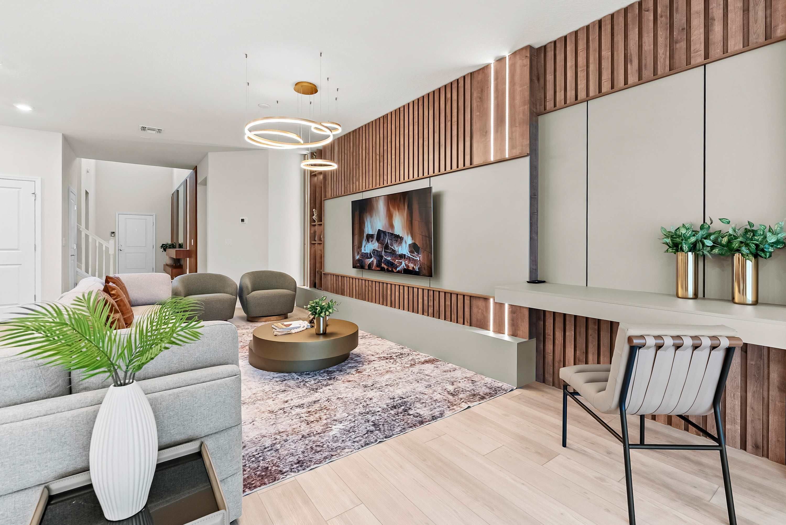 A modern living room with a sofa, chairs, a coffee table, a TV mounted on a wooden wall, and a plant on the side.