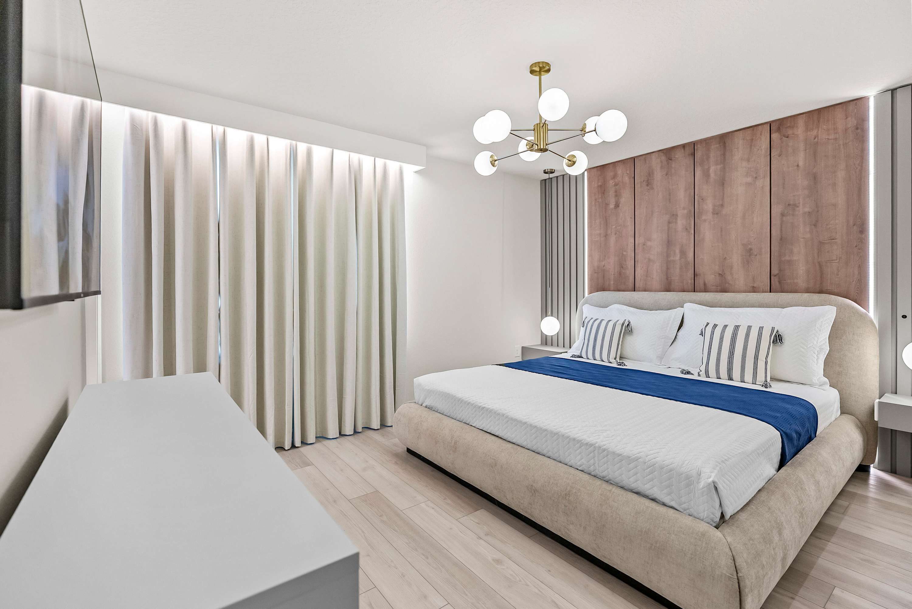 A modern bedroom with a large bed, a desk, and a wooden panel wall.