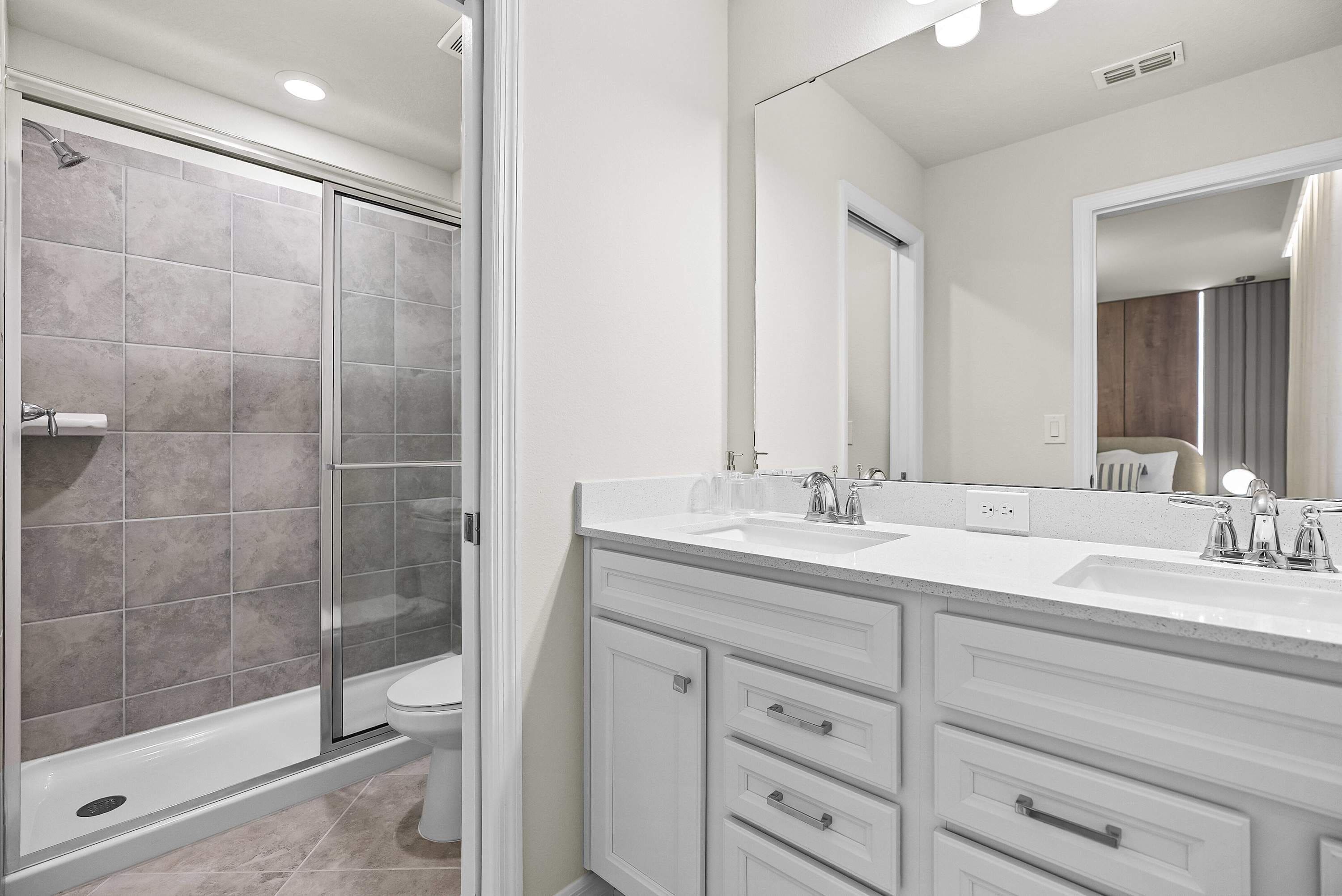 A modern bathroom with a glass-enclosed shower, a toilet, and a vanity with a large mirror.