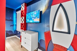 A room with a television mounted on the wall, a white dresser, and a red and blue wall design. - Luxury 8BR Themed Villa With Private Pool (Clermont)