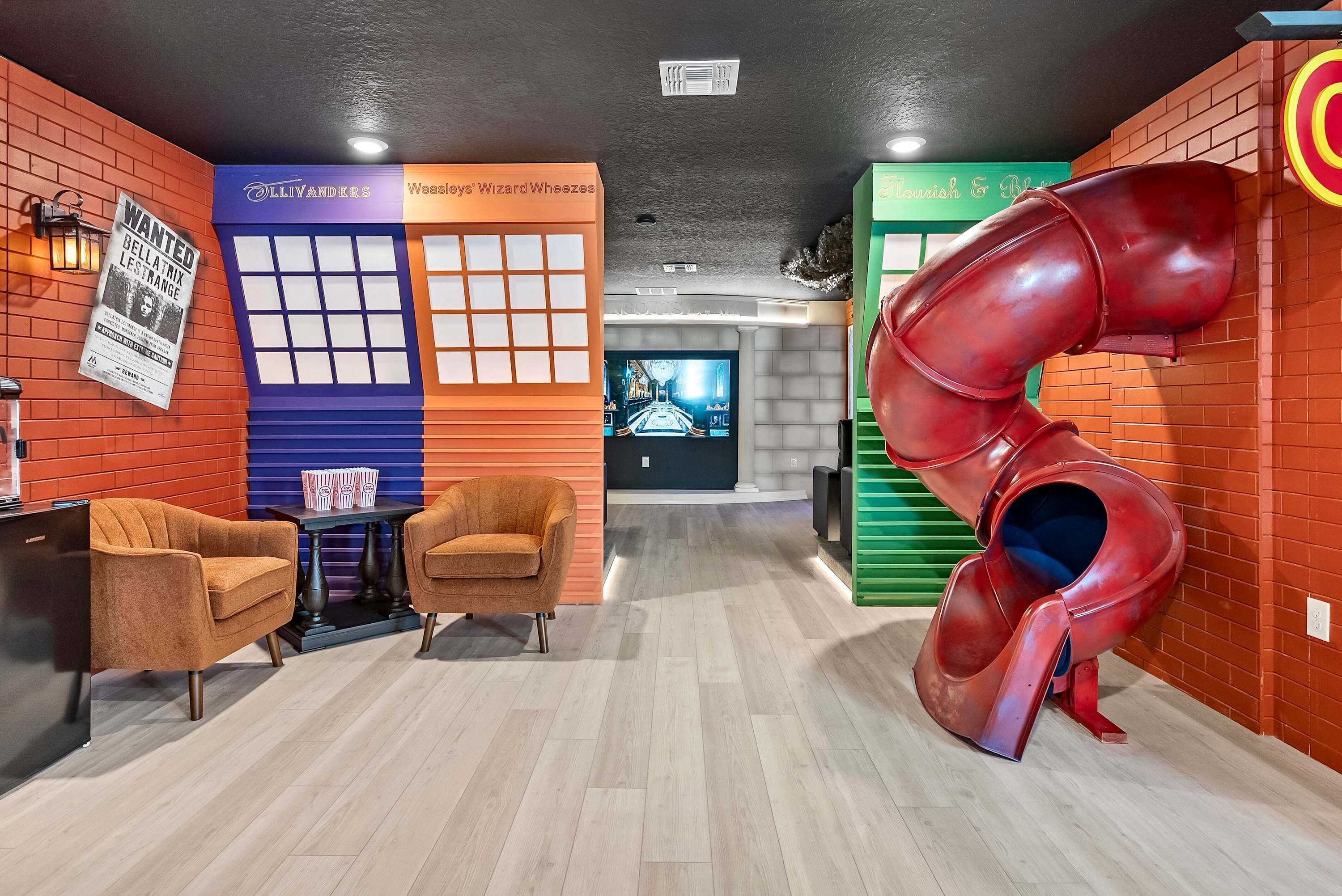 A play area with a red slide, two orange chairs, a table with popcorn boxes, and a wall with a 'Wanted' poster.