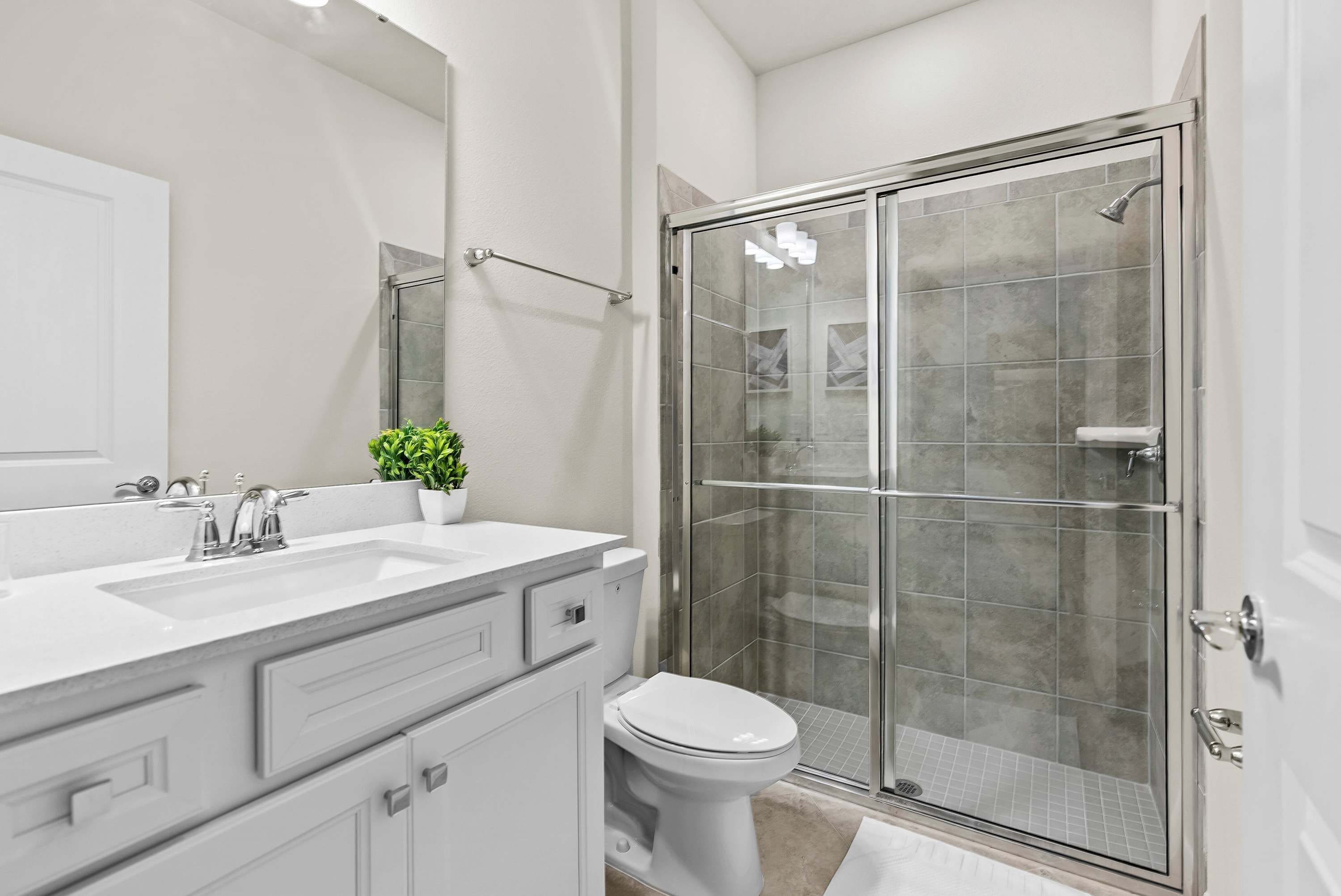 Une salle de bain moderne avec une douche à parois de verre, un lavabo blanc avec un miroir et des toilettes.
