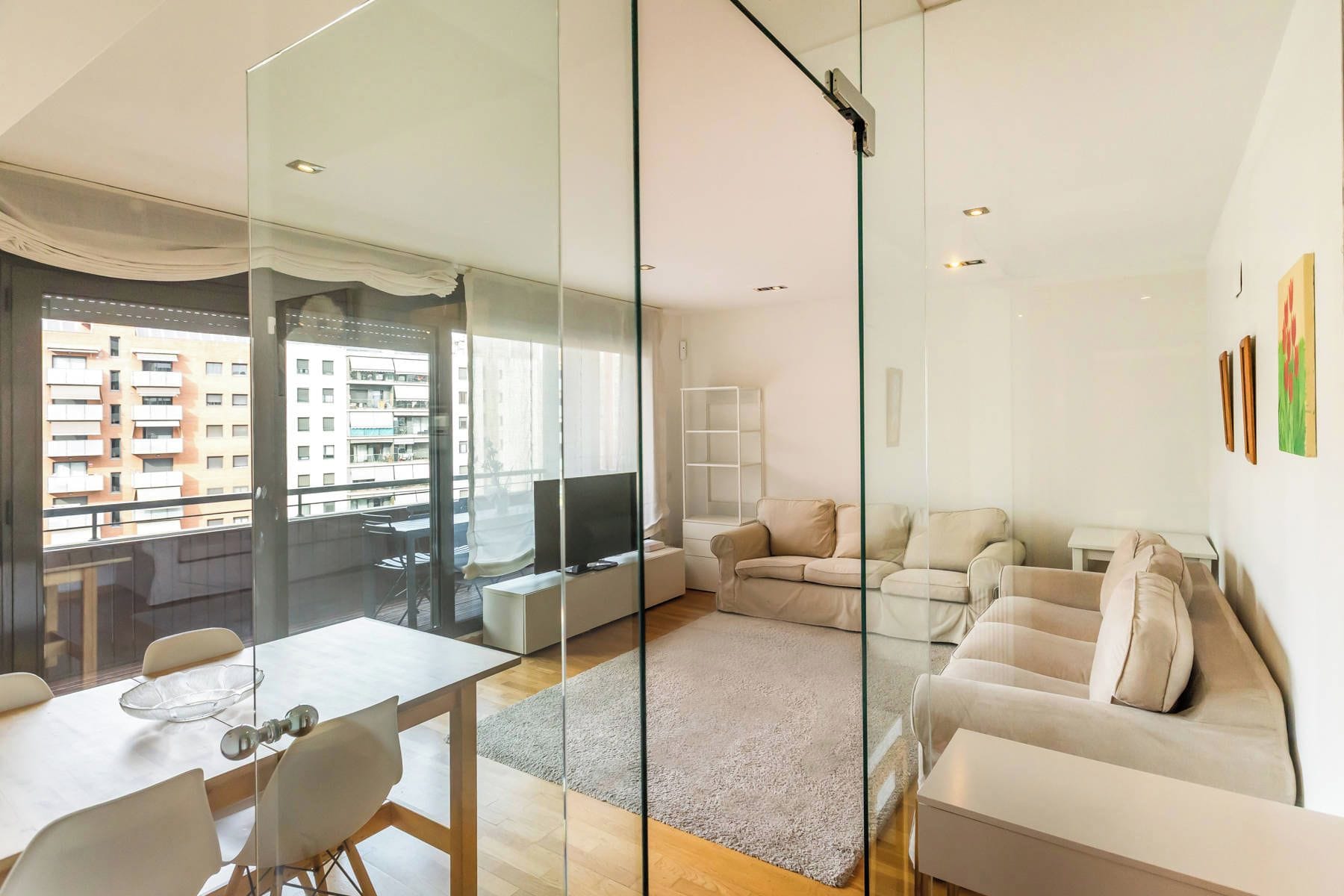 A modern living room with a glass partition, a sofa set, a TV, and a dining area with chairs and a table.