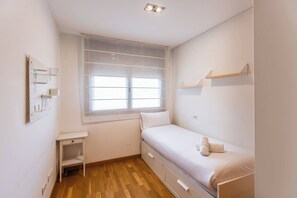Ein kleines, sauberes Zimmer mit einem Einzelbett, einem kleinen Tisch und einem Fenster mit Jalousien.