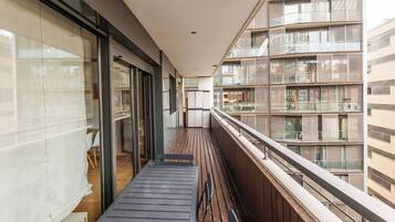 Een smal balkon met houten vloer, glazen deuren en uitzicht op omliggende gebouwen.