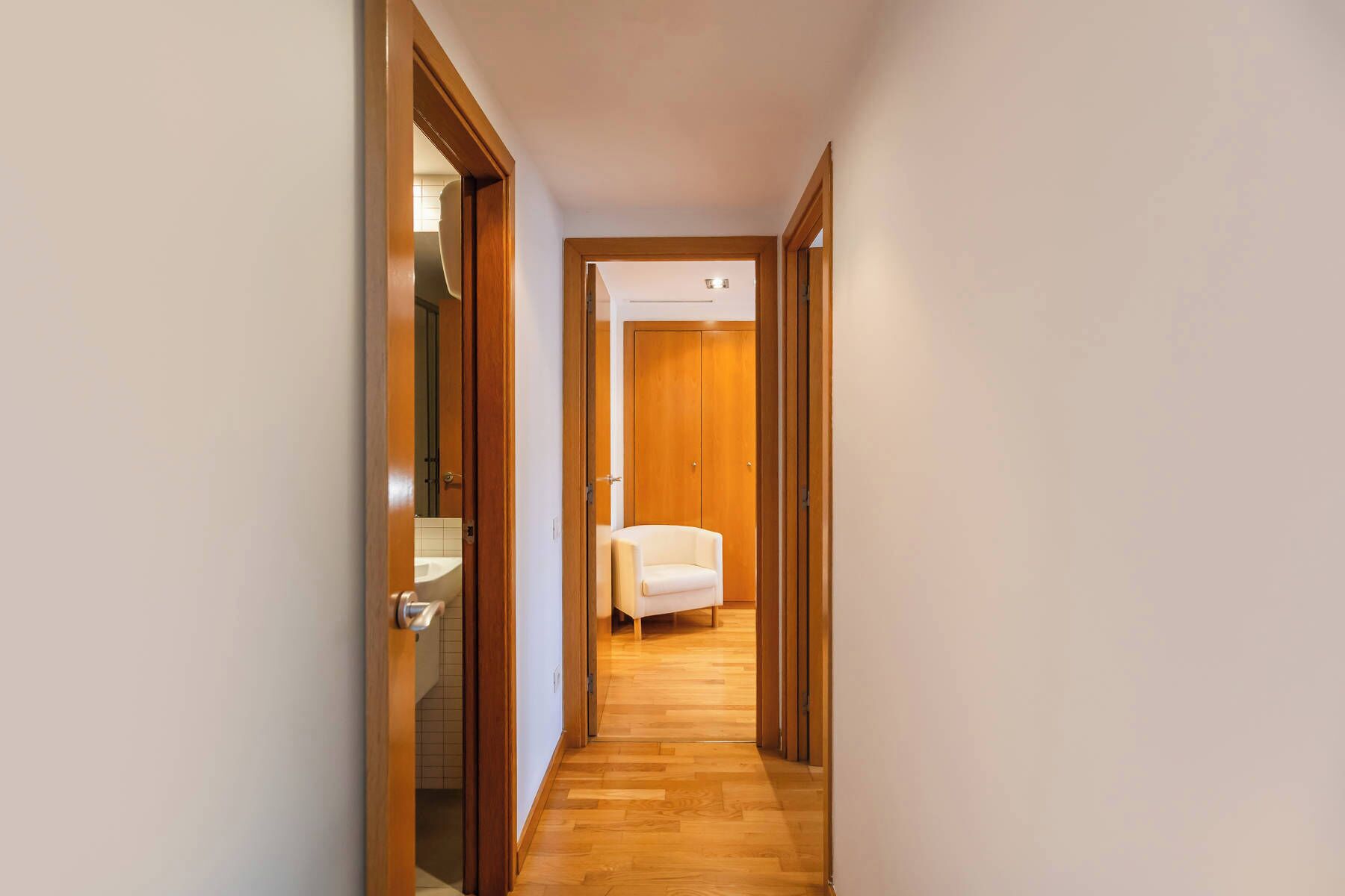 Een gang met houten deuren die leiden naar een kamer met een bed en een stoel.