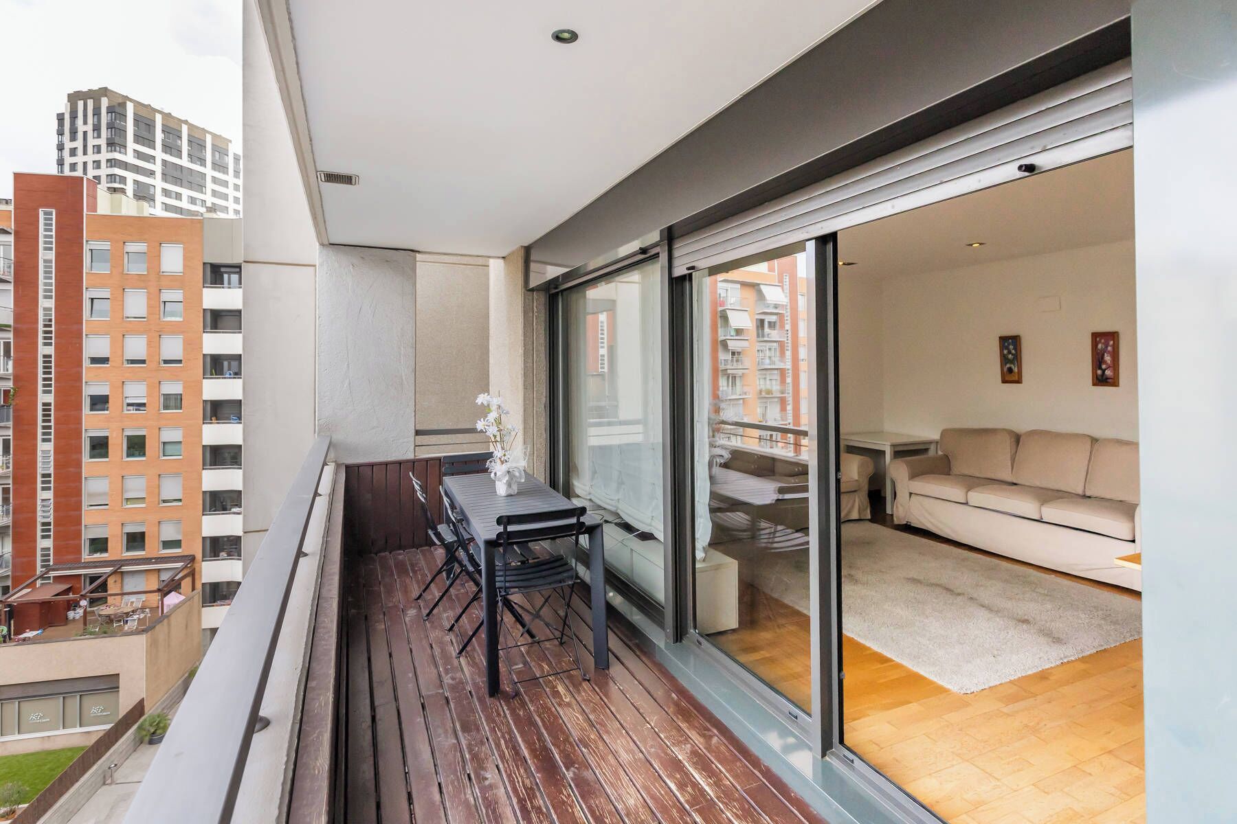 A balcony with a table and chairs, a sliding glass door leading to a living area with a sofa and a coffee table.
