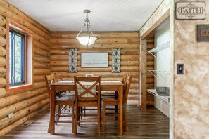 L’intérieur d’un chalet en bois, avec une table et des chaises, un luminaire suspendu et un panneau accroché au mur.
