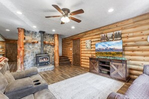 Ein Blockhaus-Interieur mit Kamin aus Stein, Deckenventilator und einem angebrachten Fernseher.