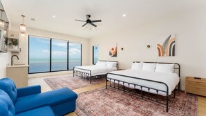 A spacious bedroom with two beds, a large window with a view of the sea, a ceiling fan, and a blue sofa. - NEW Luxury 5,500 SF Waterfront Home w/ Pool, Sleeps 28 (Port Isabel)