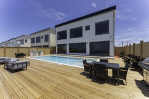 A modern outdoor pool area with a wooden deck, lounge chairs, and a barbecue grill. - 19 Spacious Bay (Port Isabel)