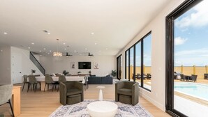 A spacious living room with a large window, a dining area, and a poolside view. - NEW Luxury 5,500 SF Waterfront Home w/ Pool, Sleeps 28 (Port Isabel)