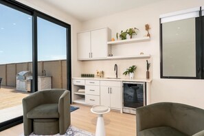 Eine moderne Küche mit weißen Schränken, einem eingebauten Ofen und einem Spülbecken. Im Wohnbereich befinden sich zwei Stühle und ein kleiner Tisch.