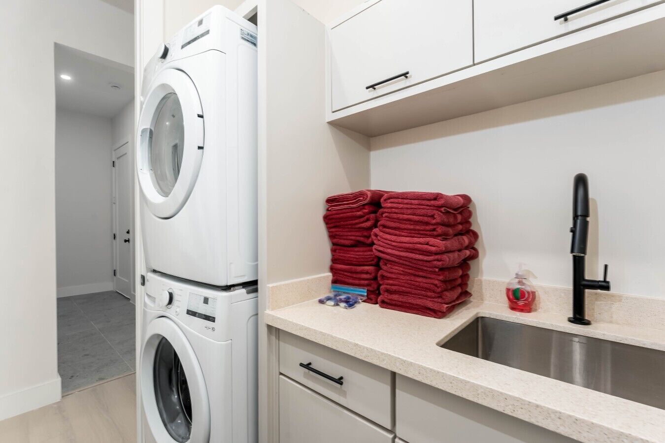 A laundry area with a washing machine, a sink, and a stack of red towels.