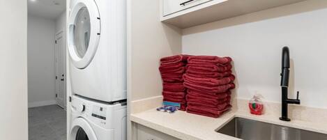 A laundry area with a washing machine, a sink, and a stack of red towels.