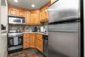 A compact kitchen with wooden cabinets, a stainless steel refrigerator, a microwave, a stove, and a dishwasher. - Swiss Mountain Escape | Pool | Hot Tub | Tennis (Midway)