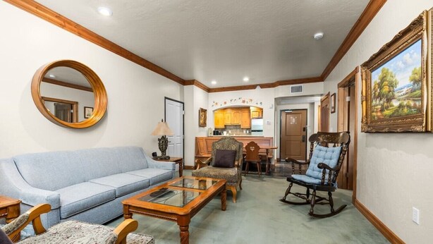 A living room with a blue sofa, a wooden coffee table, patterned chairs, a rocking chair, a round mirror, and a painting on the wall. - Swiss Mountain Escape | Pool | Hot Tub | Tennis (Midway)