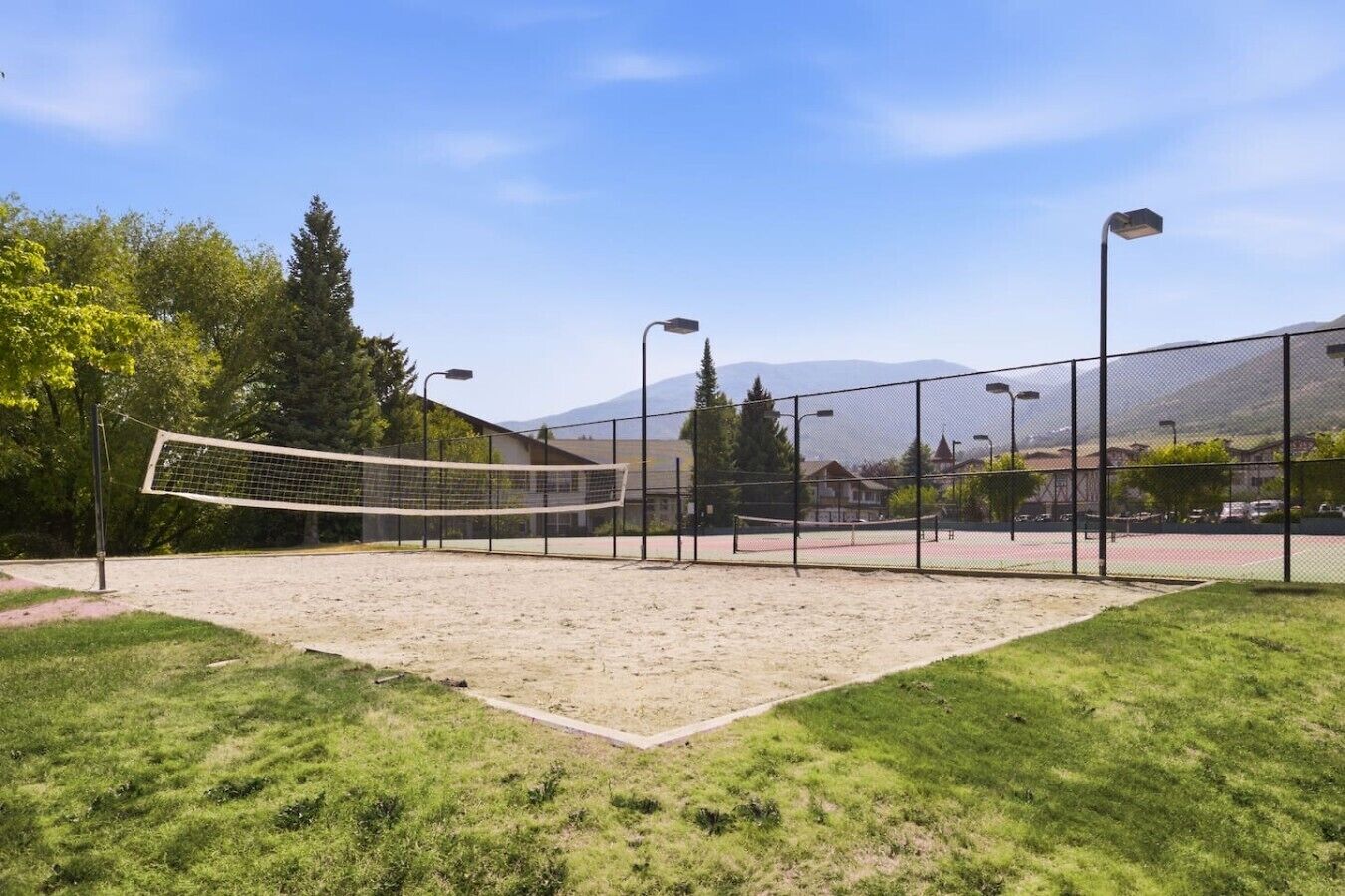 Een buitenbaan voor tennis met een net, omringd door een hek, en een berg op de achtergrond.